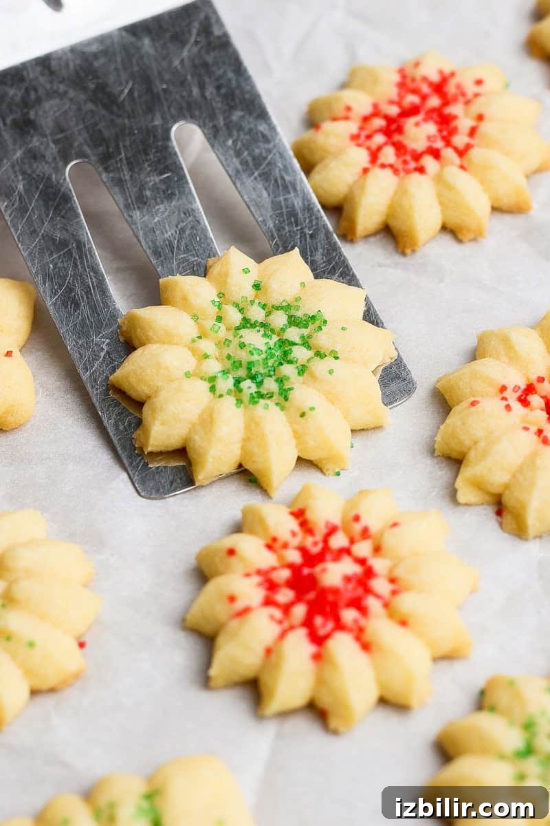 Butter cookies decorated with red and green sprinkles, arranged on a baking sheet. A spatula lifts one cookie.