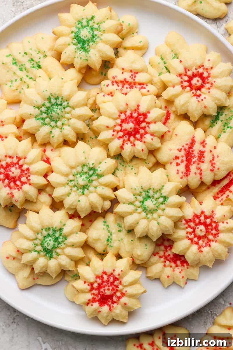A plate of flower-shaped shortbread cookies decorated with green and red sprinkles.