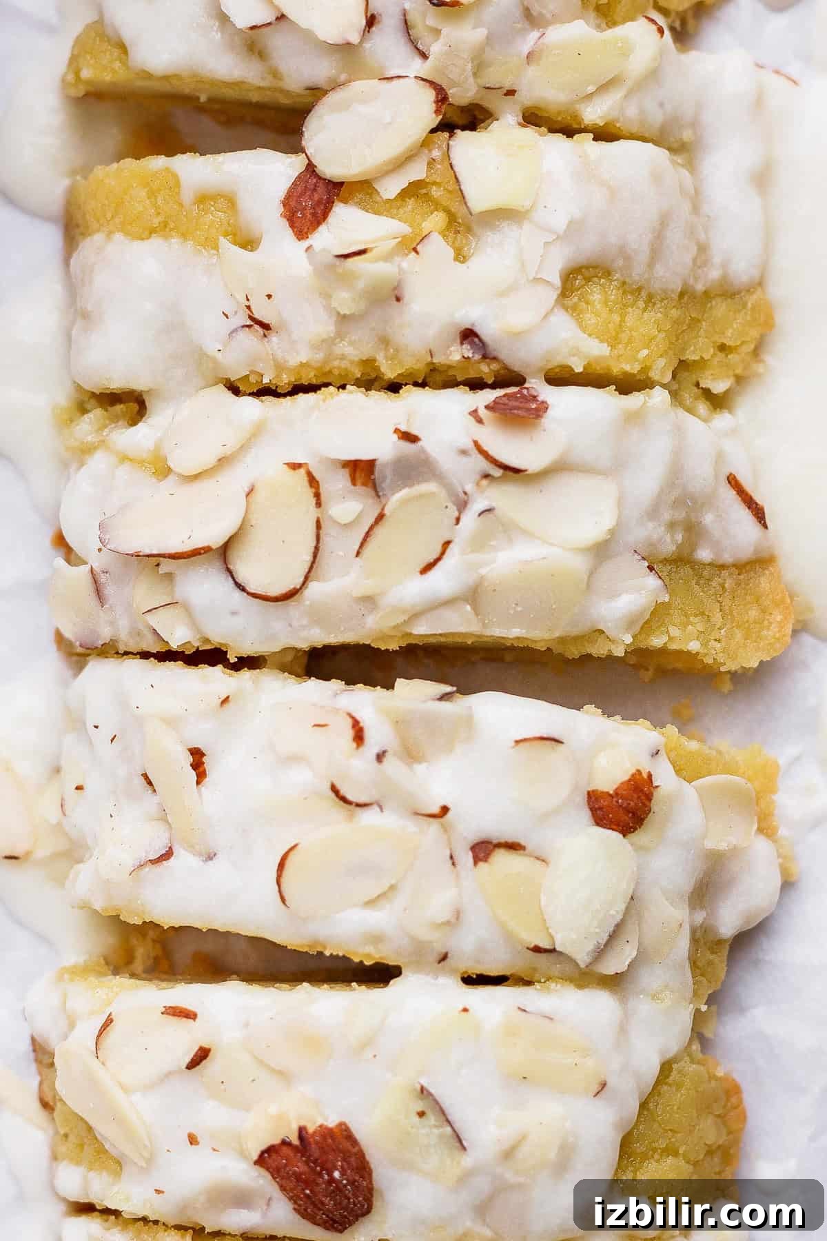 Sliced almond cake topped with white icing and sprinkled with almond slivers.