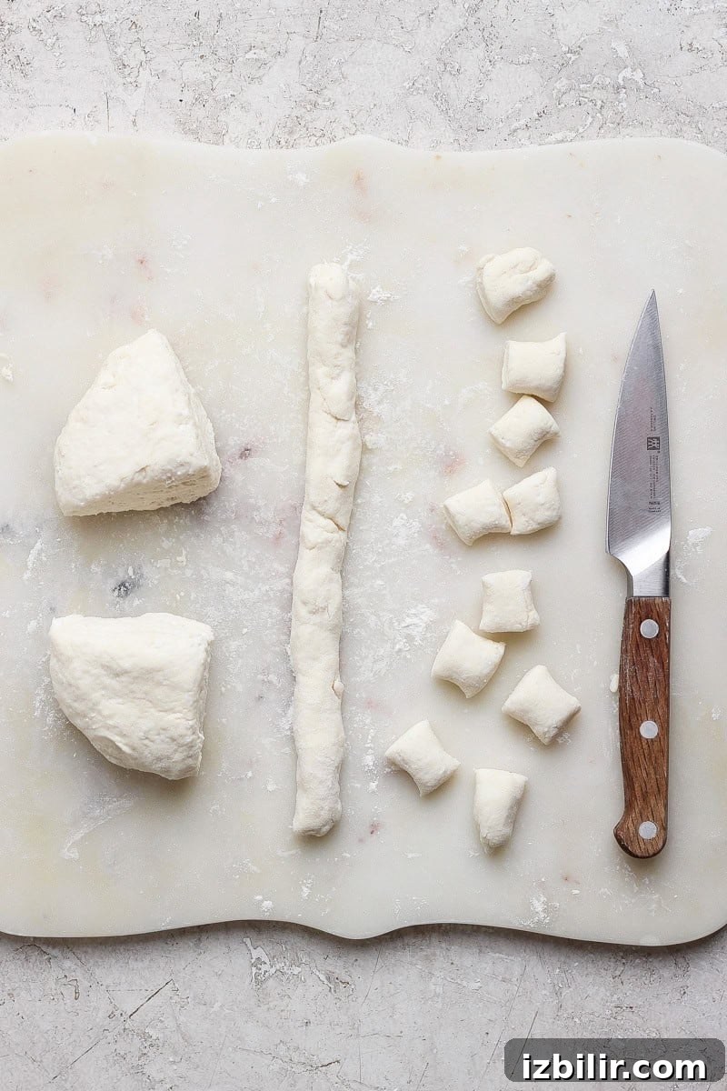 Dough being prepared on a cutting board with a knife. Dough is rolled into a log and cut into small pieces.