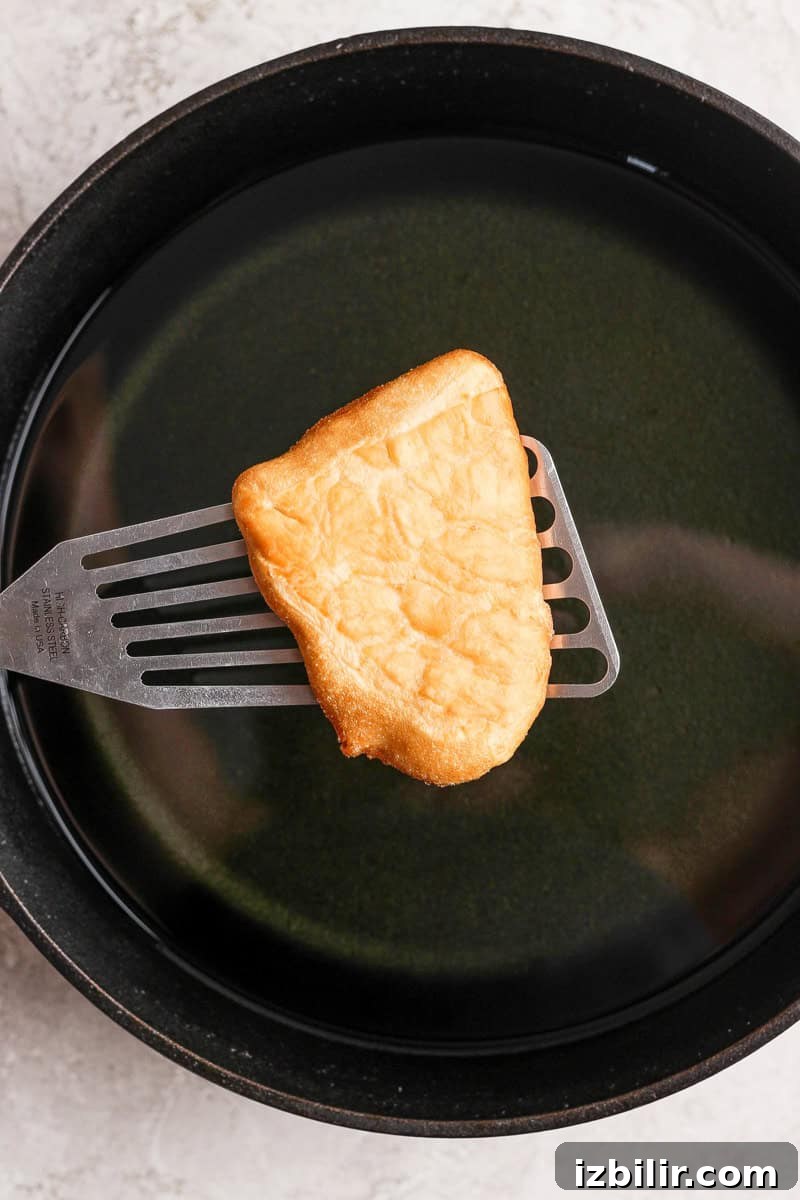 Nonna Marie's Pizza Fritta Recipe: Crispy Italian Fried Pizza 5 A piece of fried bread being lifted from a pan of oil with a metal spatula.
