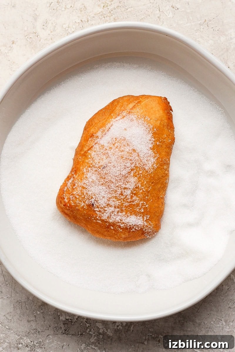 Nonna Marie's Pizza Fritta Recipe: Crispy Italian Fried Pizza 6 A sugar-covered pastry sits on a plate filled with granulated sugar.