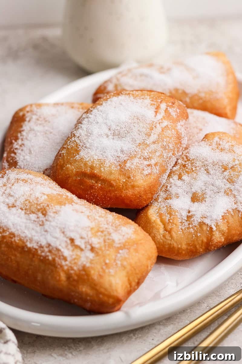 Nonna Marie's Pizza Fritta Recipe: Crispy Italian Fried Pizza 7 A plate of rectangular beignets coated with powdered sugar on a light-colored surface.