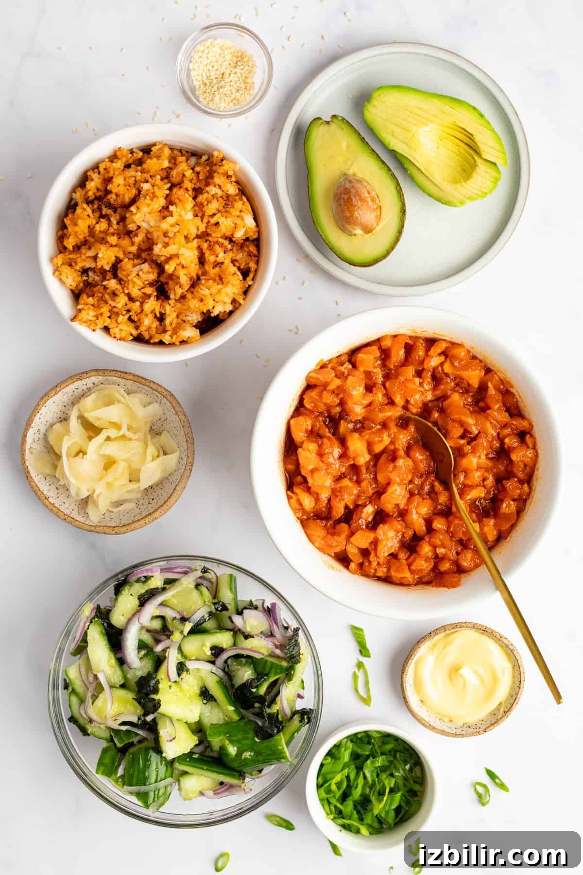 Crispy Rice Bowls with Spicy Salmon Recipe 3 Ingredients for poke bowl on a white surface: raw salmon, sliced avocado, rice, cucumber salad, pickled ginger, sliced onions, mayonnaise, sesame seeds, and chopped green onions.
