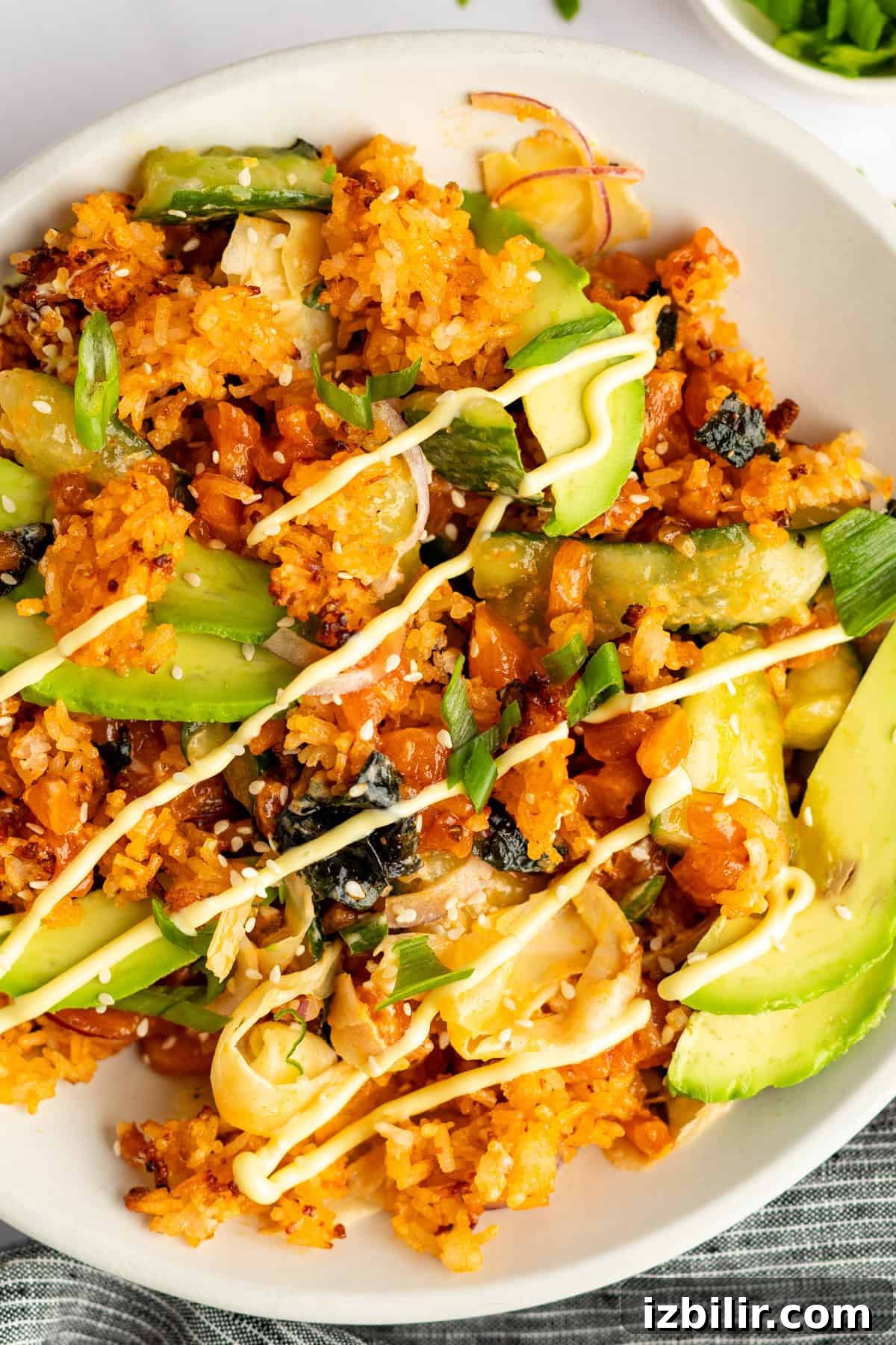 Crispy Rice Bowls with Spicy Salmon Recipe 4 A plate of seasoned rice topped with sliced avocado, cucumber, seaweed, and a drizzle of cream sauce.