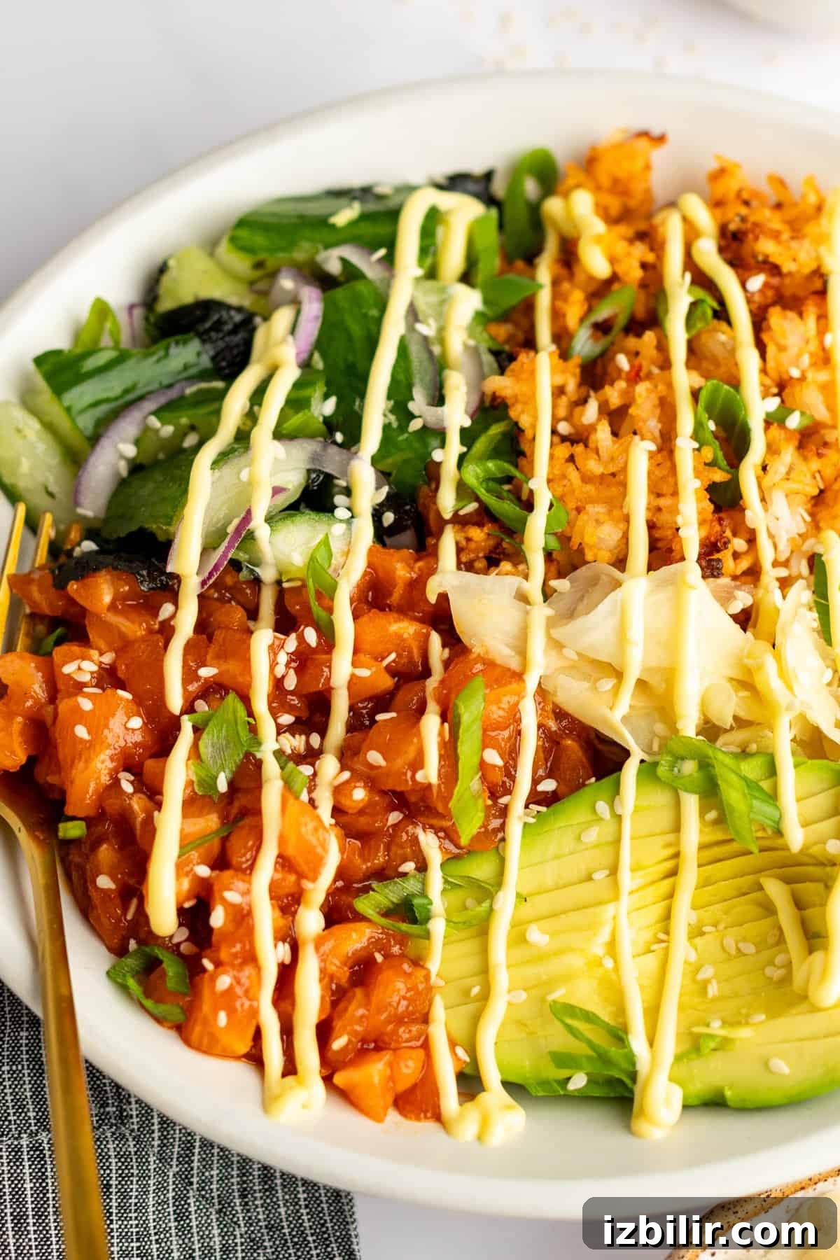 Crispy Rice Bowls with Spicy Salmon Recipe 5 A bowl with diced salmon, avocado slices, greens, onions, rice, and mayo drizzle, garnished with sesame seeds and scallions.