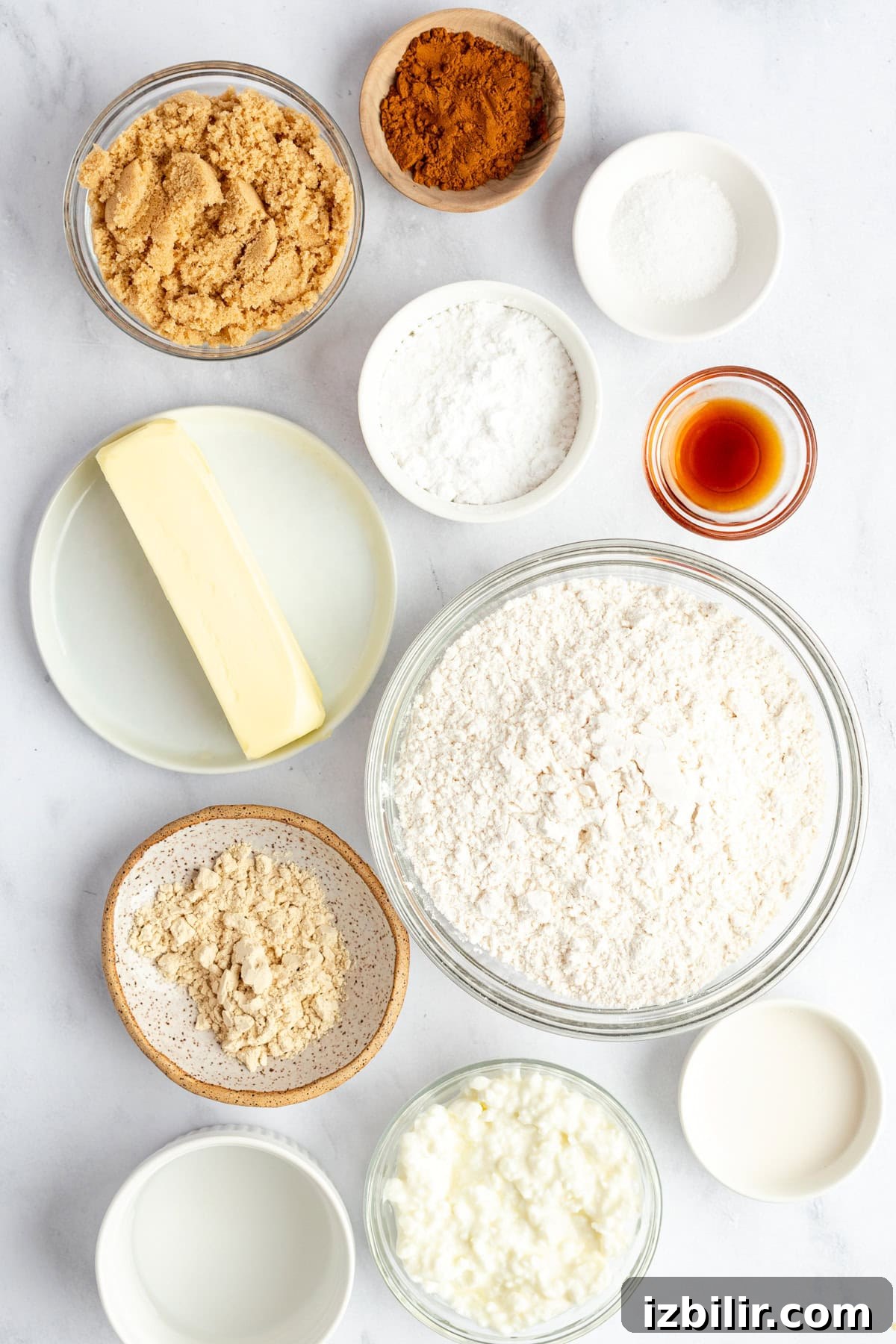 Homemade Protein Pop Tarts Recipe 4 Assorted baking ingredients on a white surface: flour, brown sugar, butter, cocoa powder, baking powder, vanilla extract, sour cream, and milk in bowls and plates.
