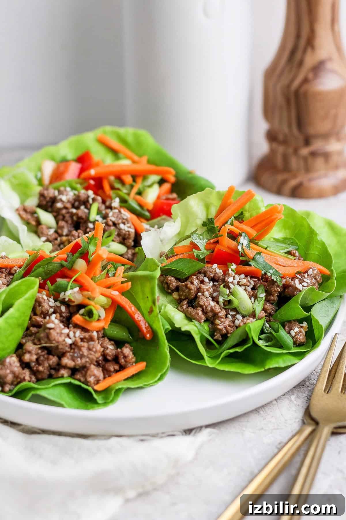 Korean Beef Lettuce Wraps with Gochujang Glaze 5 Lettuce wraps filled with minced meat, sliced carrots, sesame seeds, and green onions on a white plate.