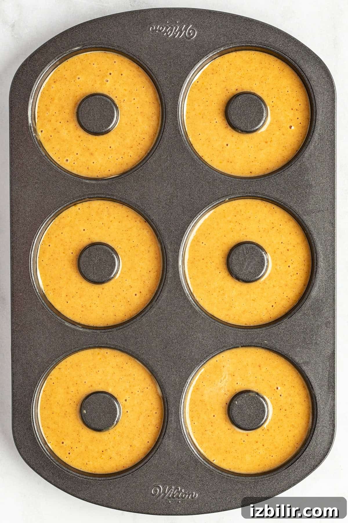 A six-cavity donut baking pan filled with pumpkin batter, ready for baking.