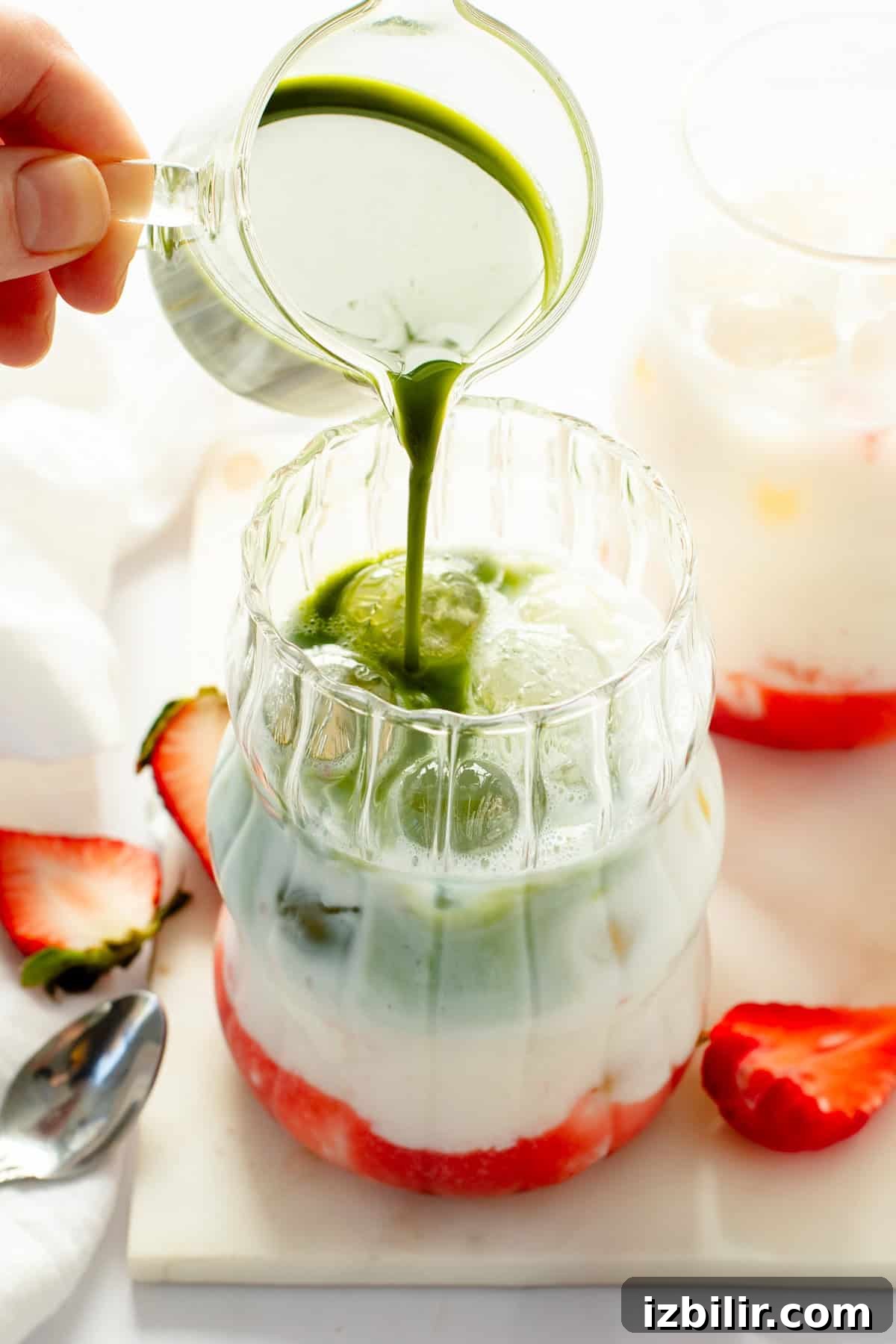 Iced Strawberry Matcha Protein Smoothie Recipe 5 Milk being poured into a glass with strawberries and green liquid.