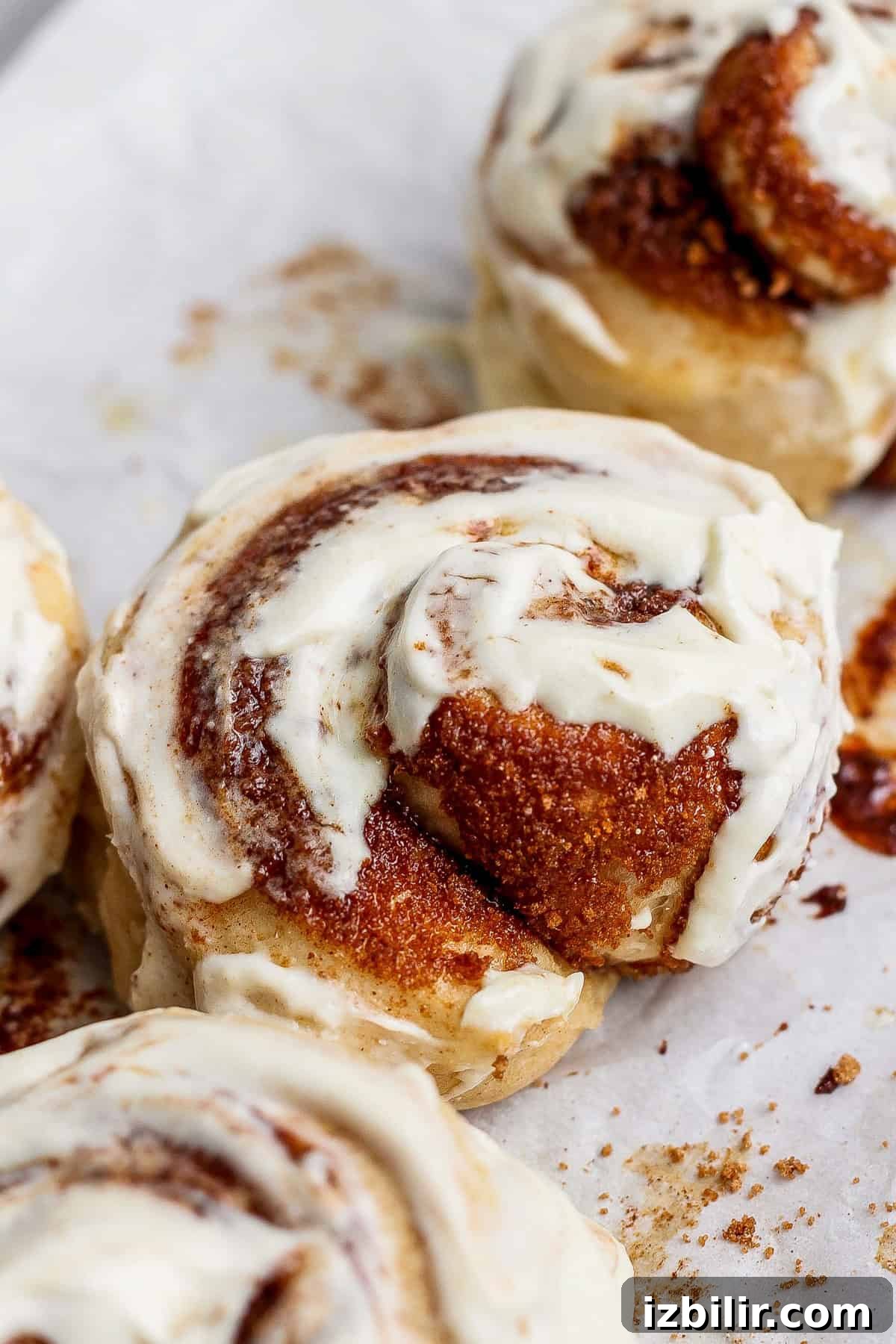 Small-Batch High-Protein Cinnamon Roll Recipe 2 Close-up of protein cinnamon rolls topped with creamy white icing on a parchment-lined surface.