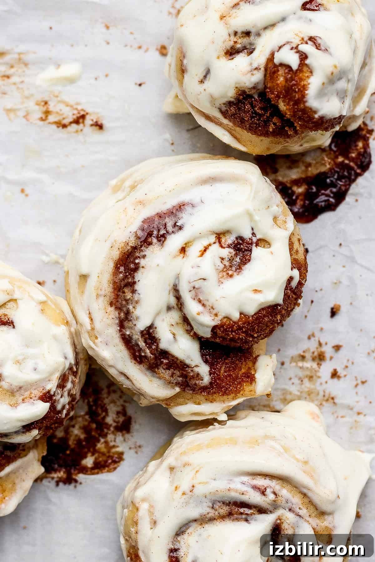 Small-Batch High-Protein Cinnamon Roll Recipe 4 Top view of four cinnamon rolls with white icing on a parchment paper background.