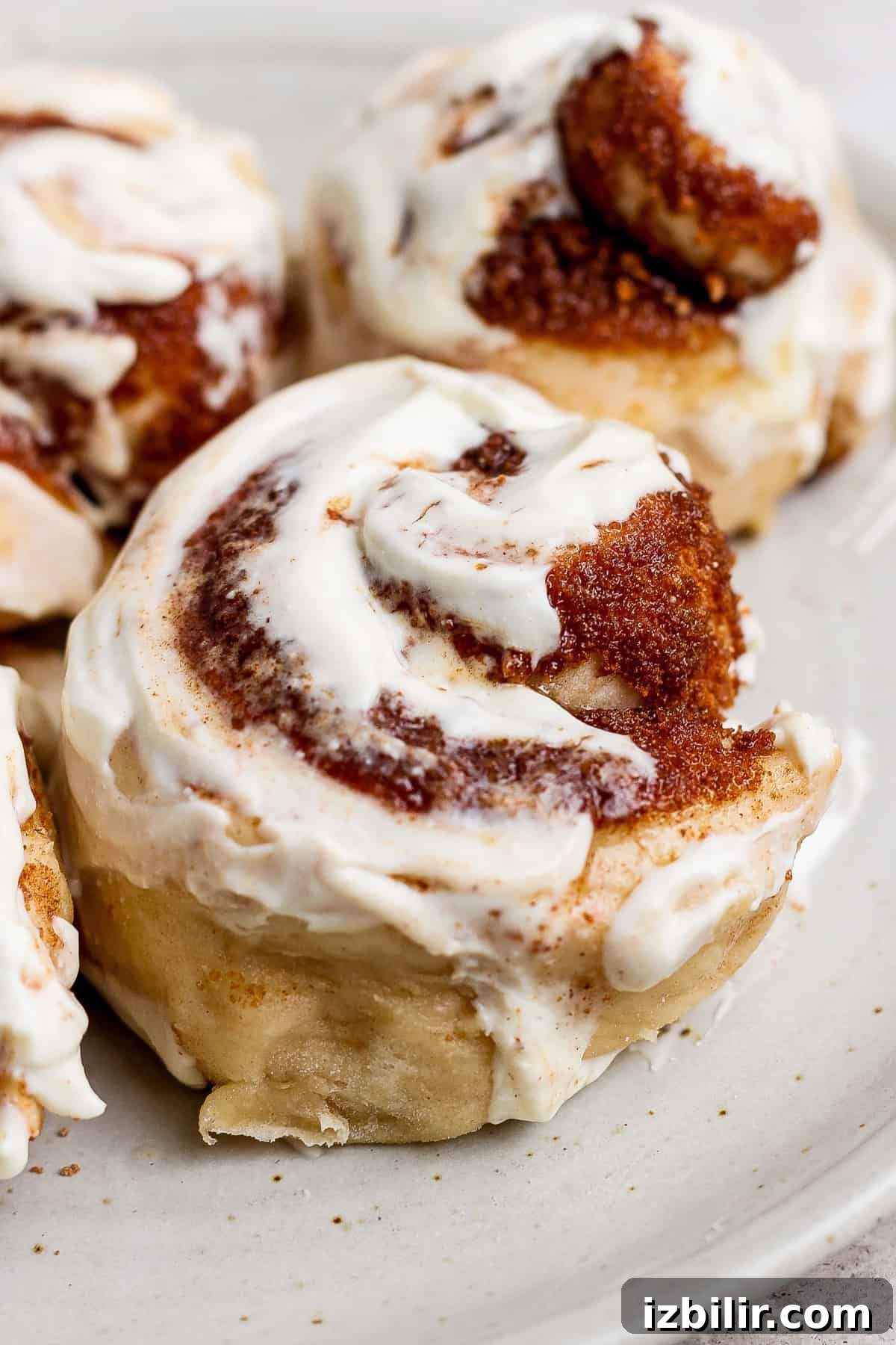 Small-Batch High-Protein Cinnamon Roll Recipe 5 Close-up of freshly baked cinnamon rolls with creamy frosting on a white plate.
