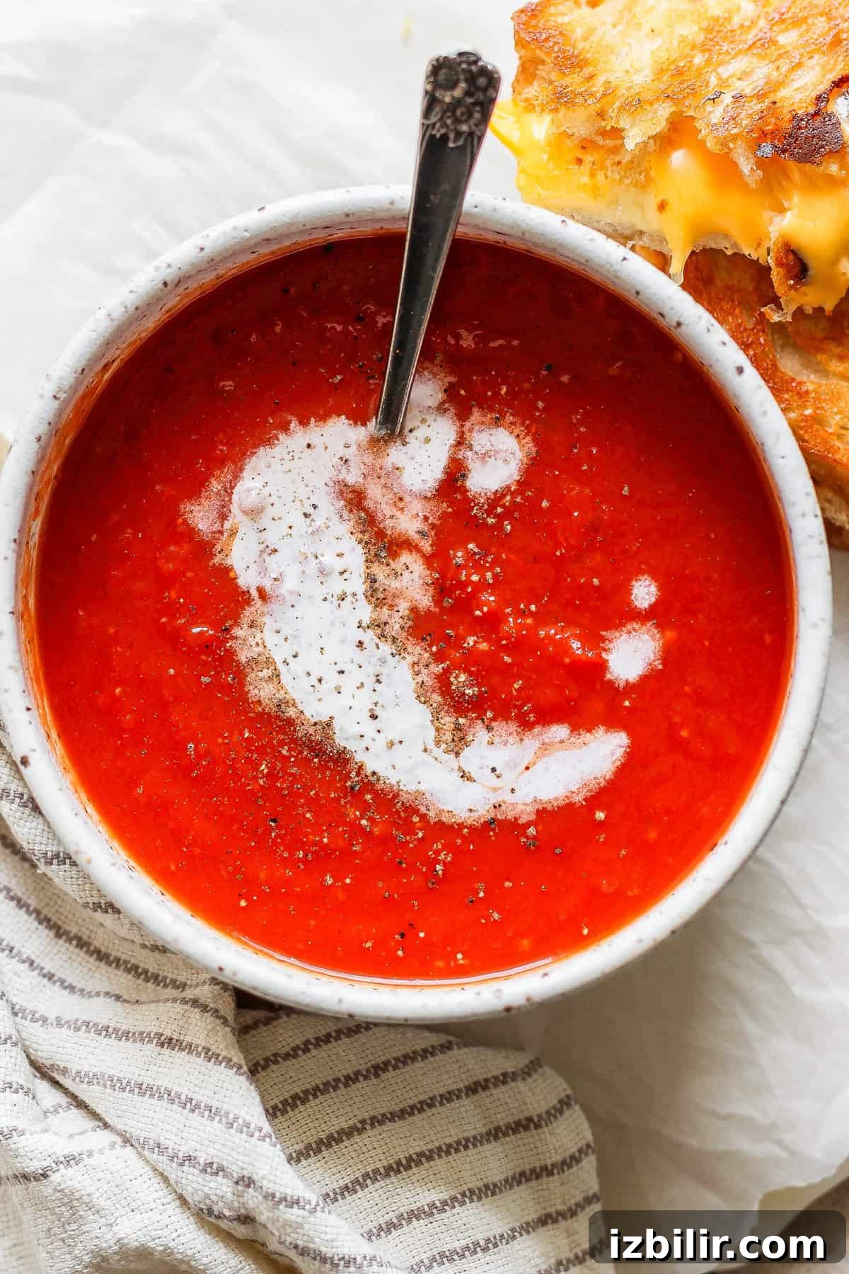 A bowl of creamy tomato soup topped with pepper, paired with a melty grilled cheese sandwich.