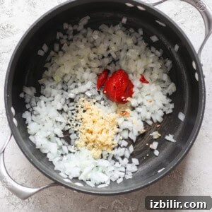 Chopped onions, minced garlic, and dollops of tomato paste in a black pot.