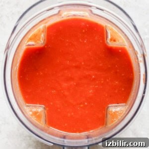 Top view of a blender containing smooth red tomato sauce.