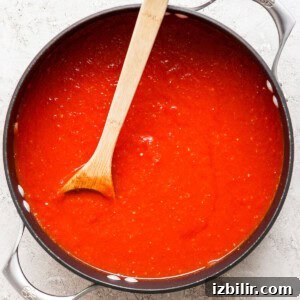 A pot filled with rich tomato sauce and a wooden spoon resting inside.