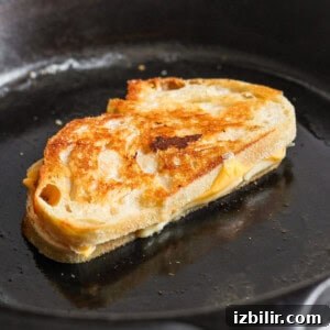 A grilled cheese sandwich sizzles in a skillet with a golden crust.