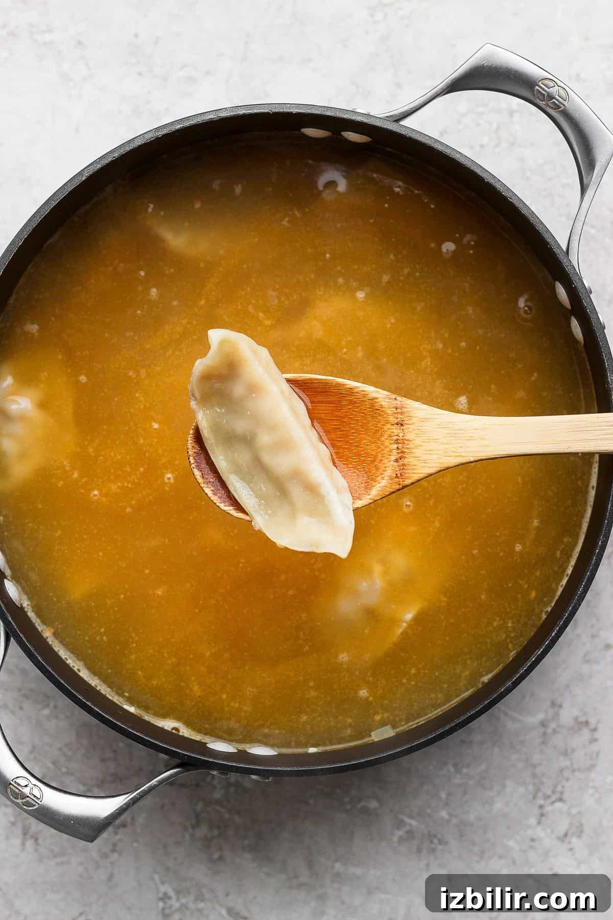 Zesty Lemon Wonton Soup Recipe 3 A pot of broth with a wooden spoon holding a dumpling above the liquid.