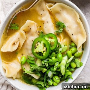 Zesty Lemon Wonton Soup Recipe 4 A bowl of soup with dumplings, topped with sliced jalapeños, edamame, green onions, and cilantro.