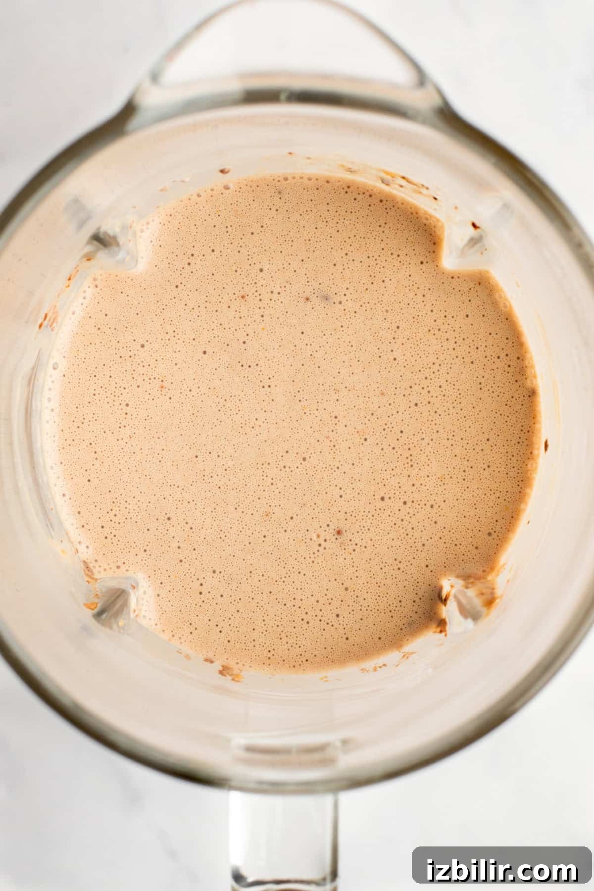 A top view of a blender containing a smooth, light brown liquid mixture.