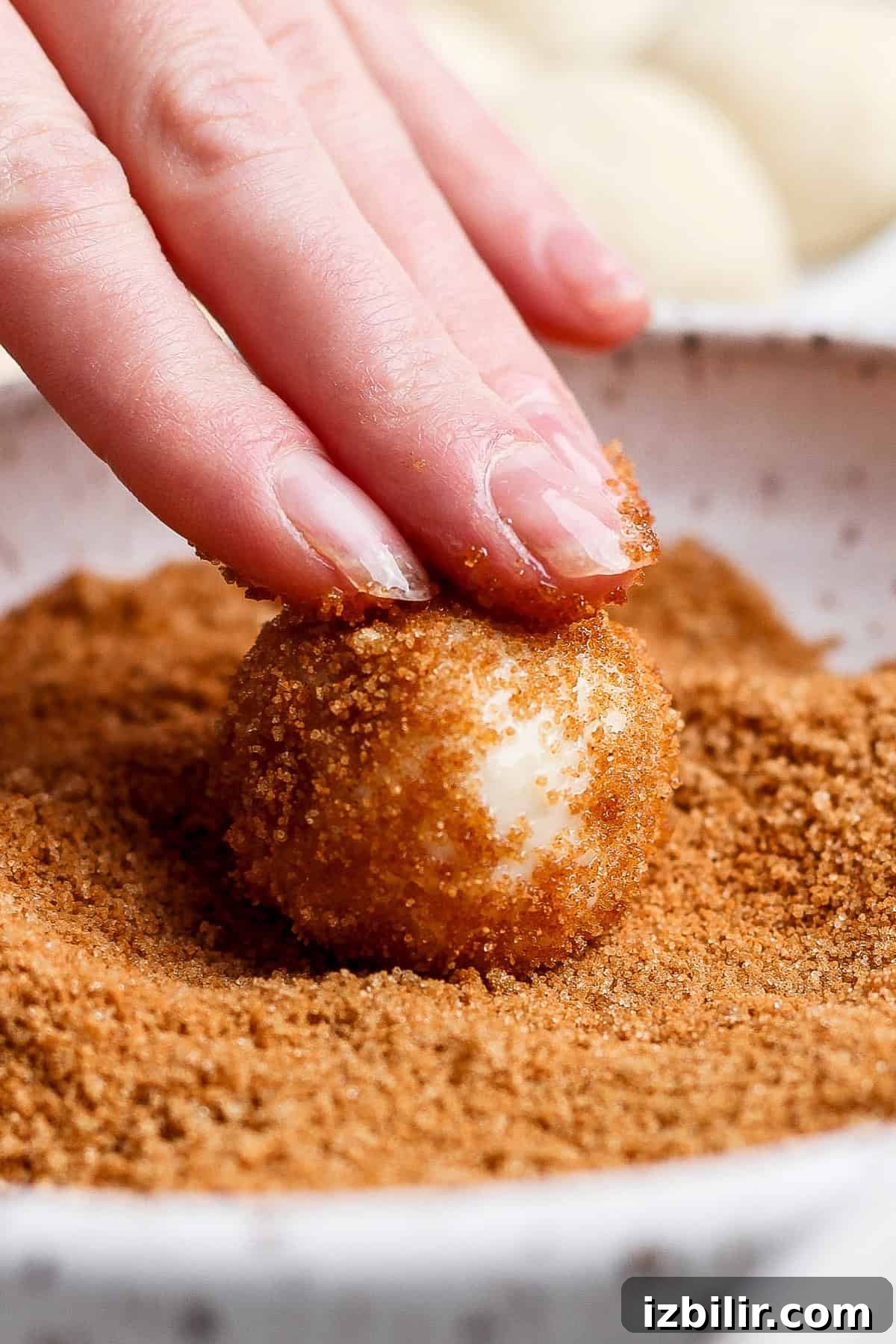 Air Fryer Protein Monkey Bread Recipe 4 A hand rolls a dough ball in a bowl of brown sugar topping.
