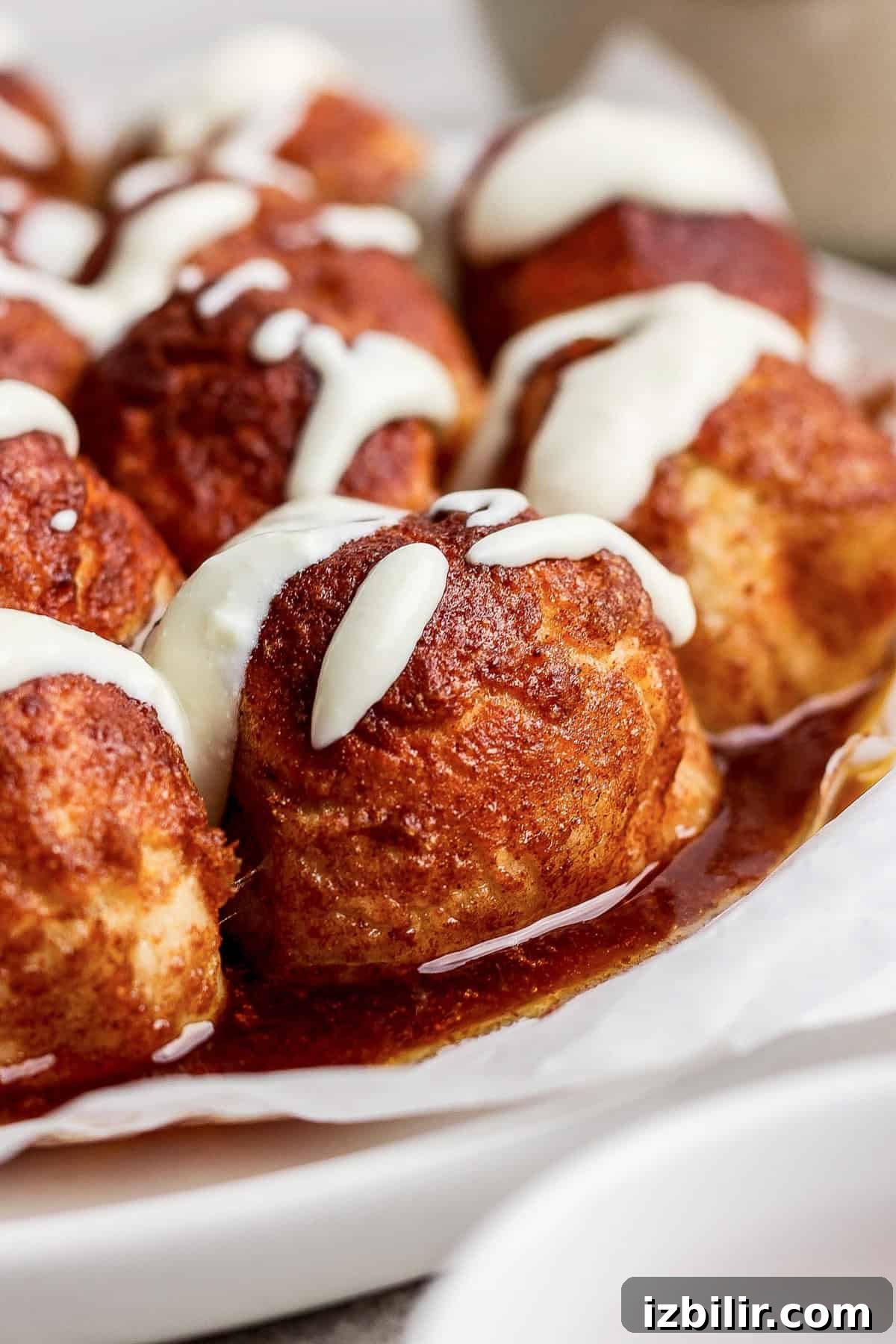 Air Fryer Protein Monkey Bread Recipe 7 Close-up of cinnamon rolls topped with white icing, arranged on wax paper.
