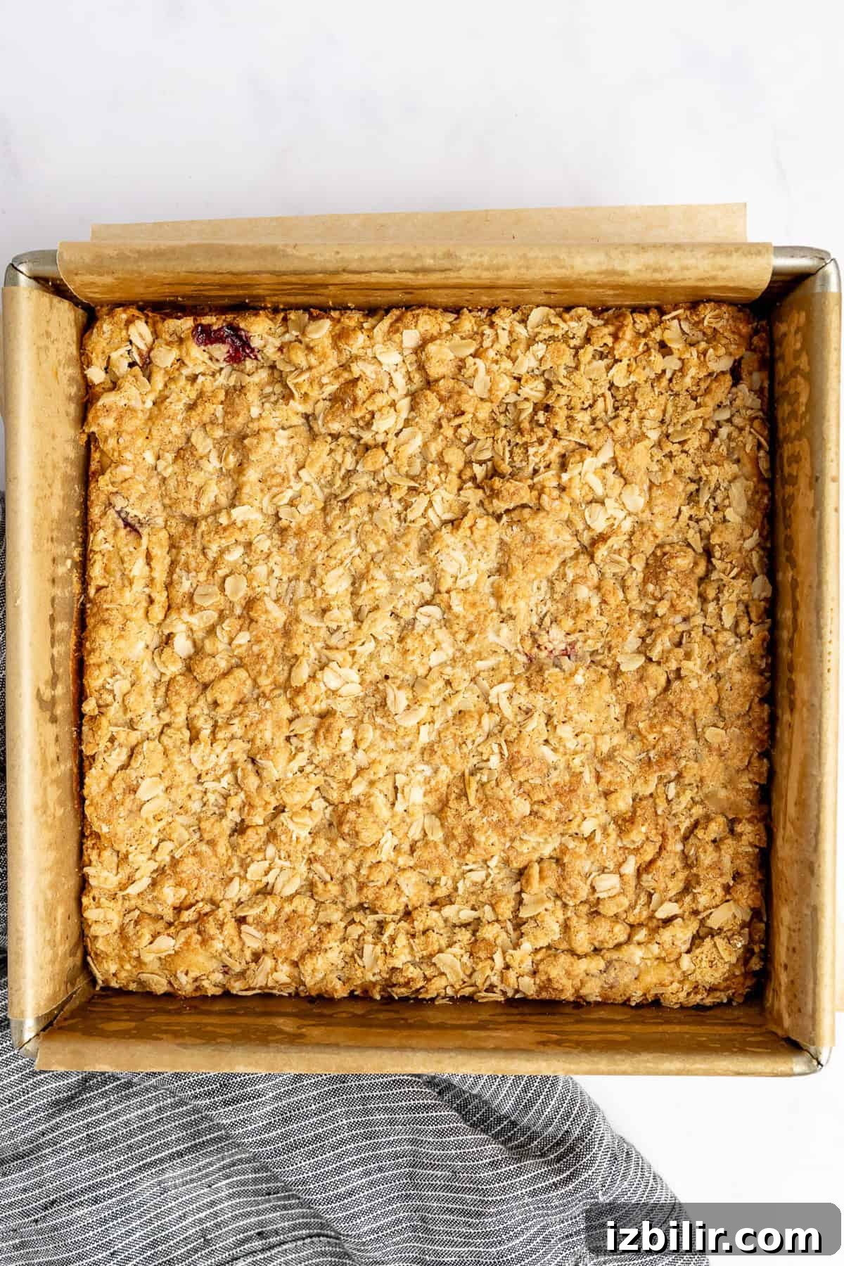 Square baking dish with a golden-brown baked oat crumble on parchment paper, resting on a light surface.