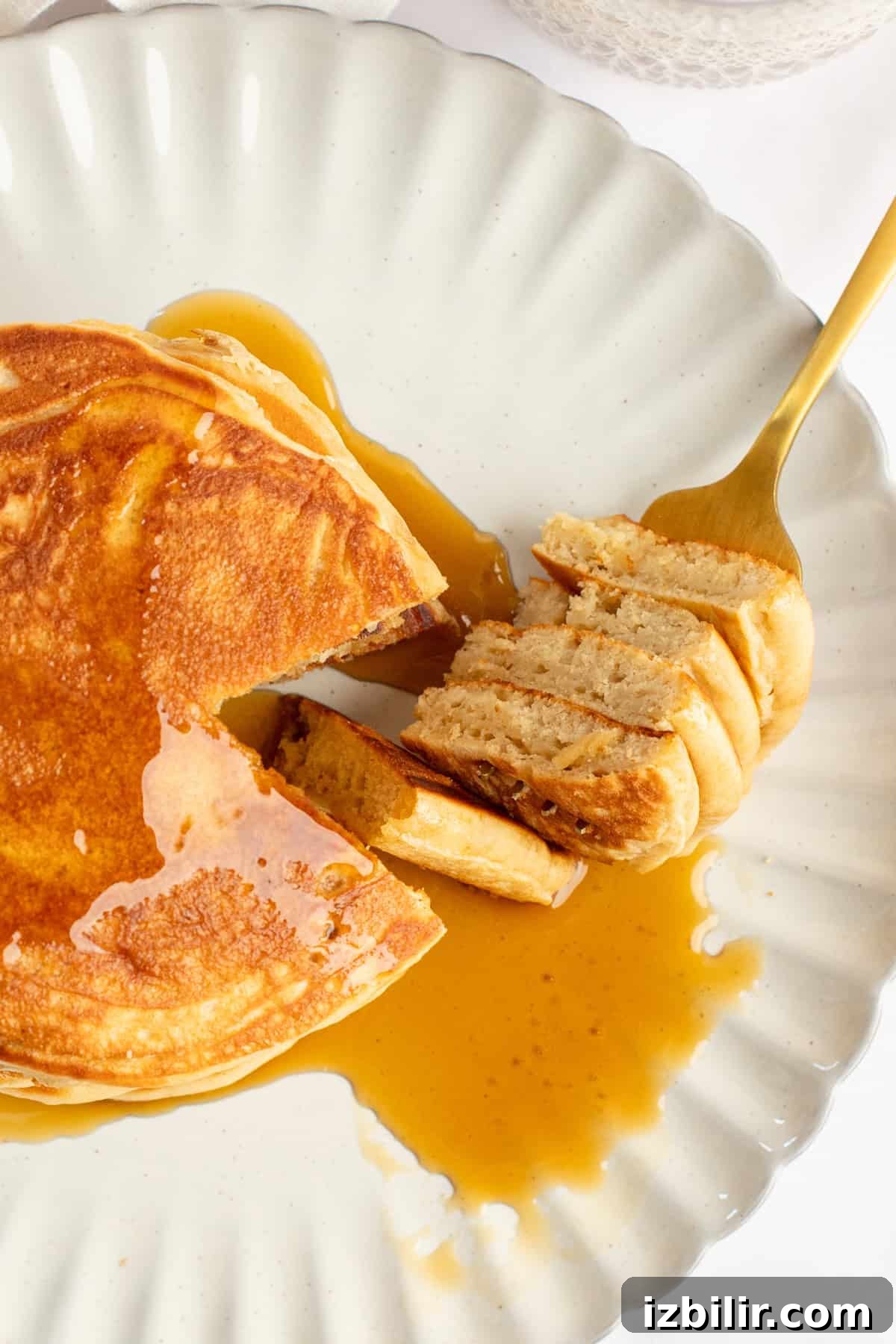 A plate of pancakes with syrup, partially eaten, sits on a white dish. A fork holds a cut portion of the pancakes.