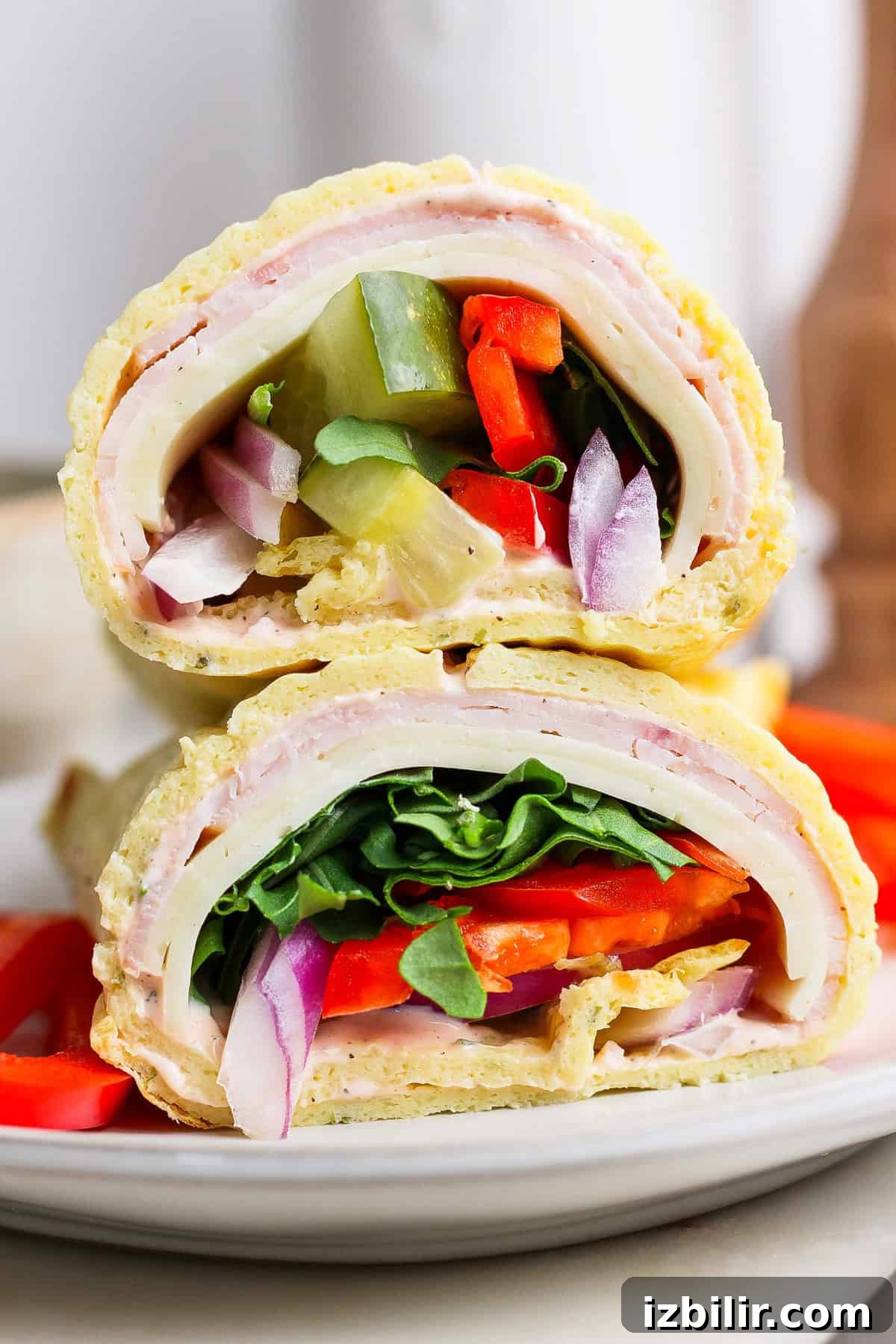 Protein-Packed Cottage Cheese Wraps Recipe 5 Close-up of two sandwich halves stacked, featuring layers of turkey, cheese, spinach, tomato, onion, and green pepper on a rolled flatbread.