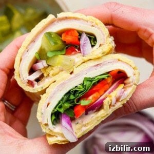 Protein-Packed Cottage Cheese Wraps Recipe 6 Hands holding a delicious cottage cheese wrap filled with turkey, lettuce, tomato, pickles, red onion, and spinach.