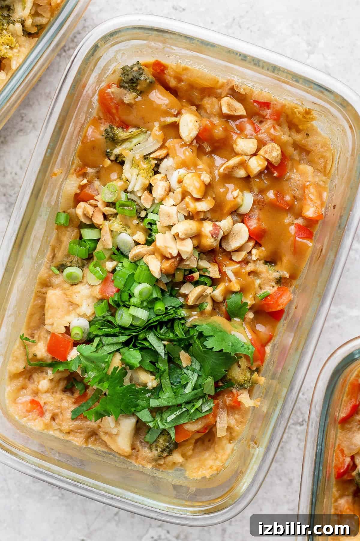 Baked Peanut Butter Chicken for Meal Prep 4 A glass container holds a colorful salad topped with chopped peanuts, green onions, and cilantro, accompanied by tender slices of peanut chicken, resting elegantly on a light textured surface.