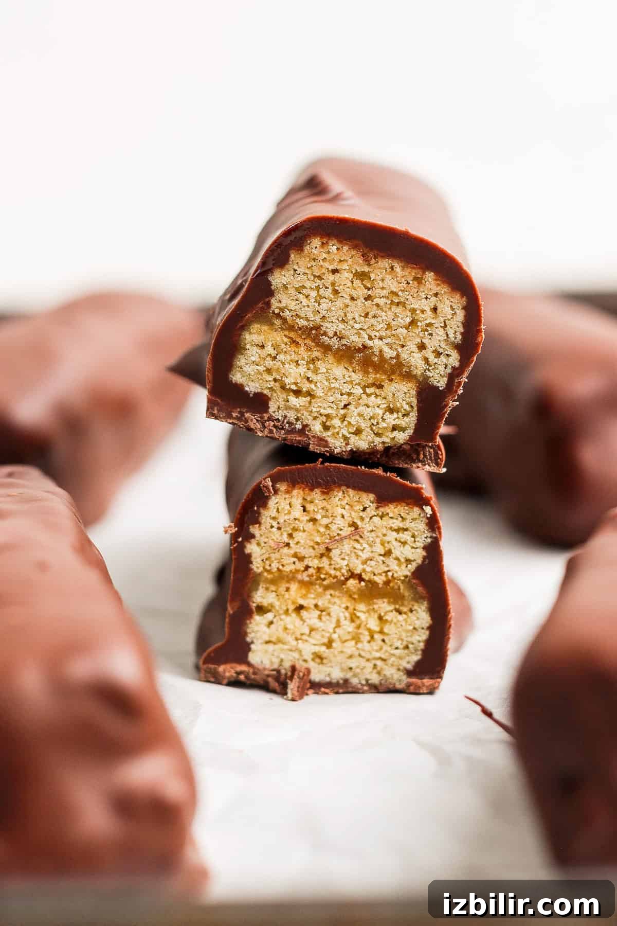 High-Protein Peanut Butter Twix Bars Recipe 2 Two chocolate-coated biscuit bars stacked with one bisected, revealing a layered interior on a white surface.