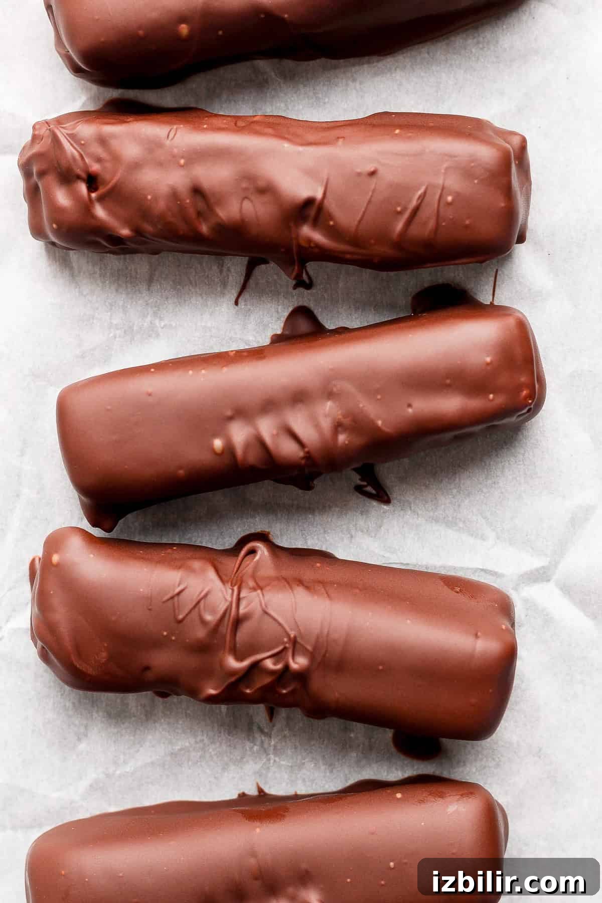 High-Protein Peanut Butter Twix Bars Recipe 9 Five chocolate-coated bars arranged in a row on parchment paper.