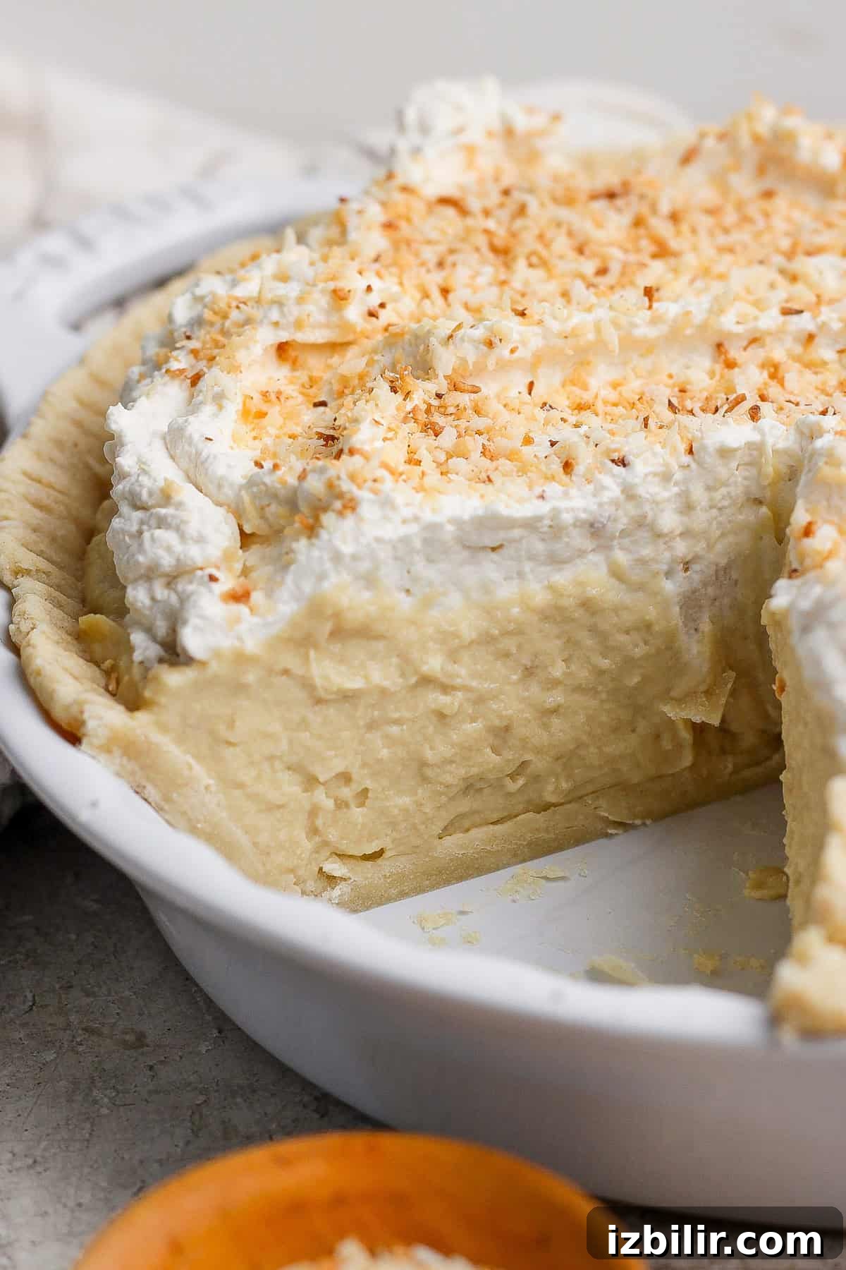 Protein Packed Pie Crust Recipe 5 A creamy pie with a slice removed, topped with whipped cream and toasted coconut flakes, in a white pie dish.