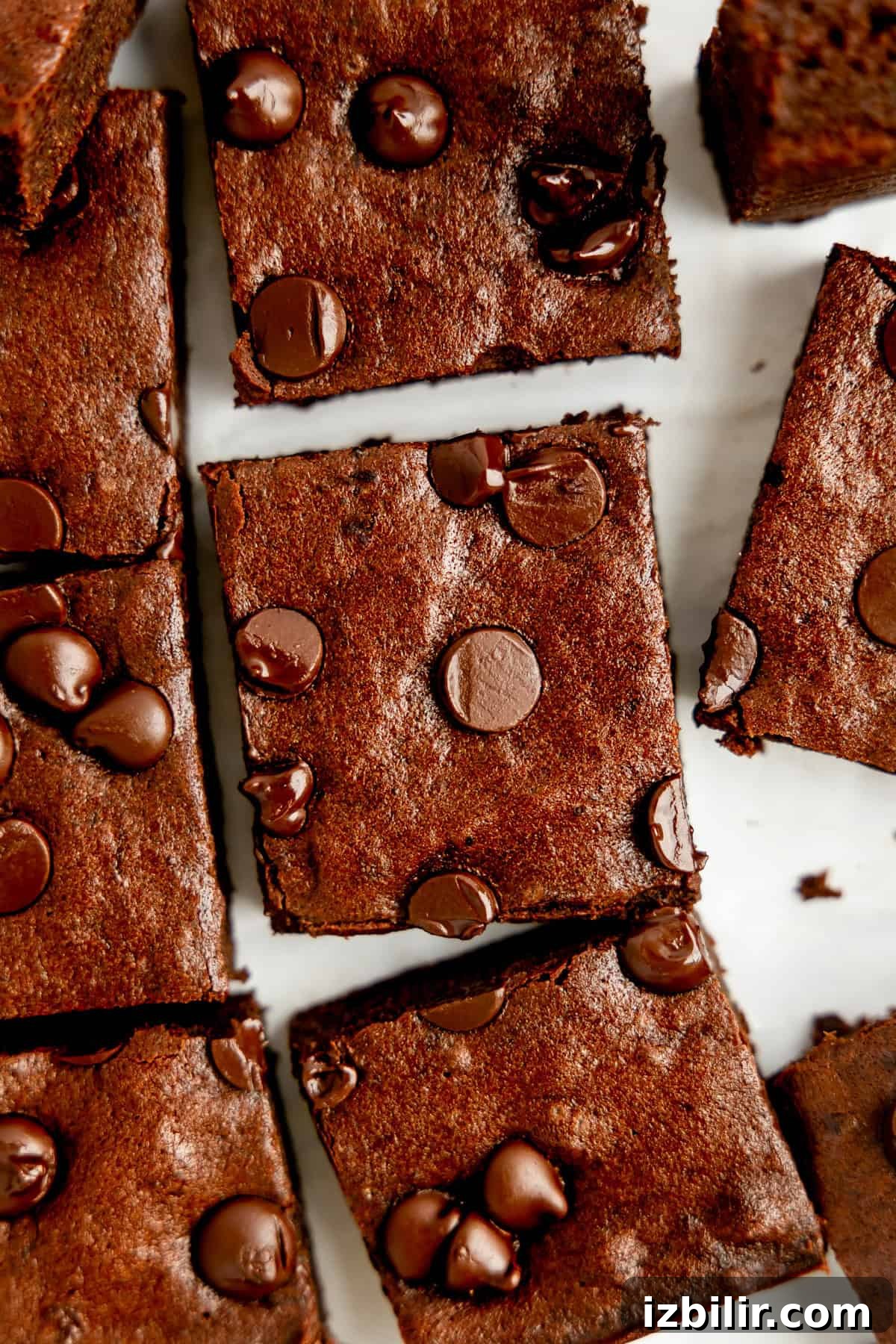 Close-up of sliced chocolate brownies topped with chocolate chips on a white surface.