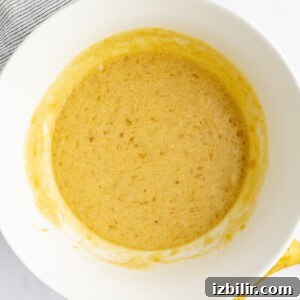 Bowl of mashed banana mixture, with a partially visible ripe banana and striped cloth nearby.