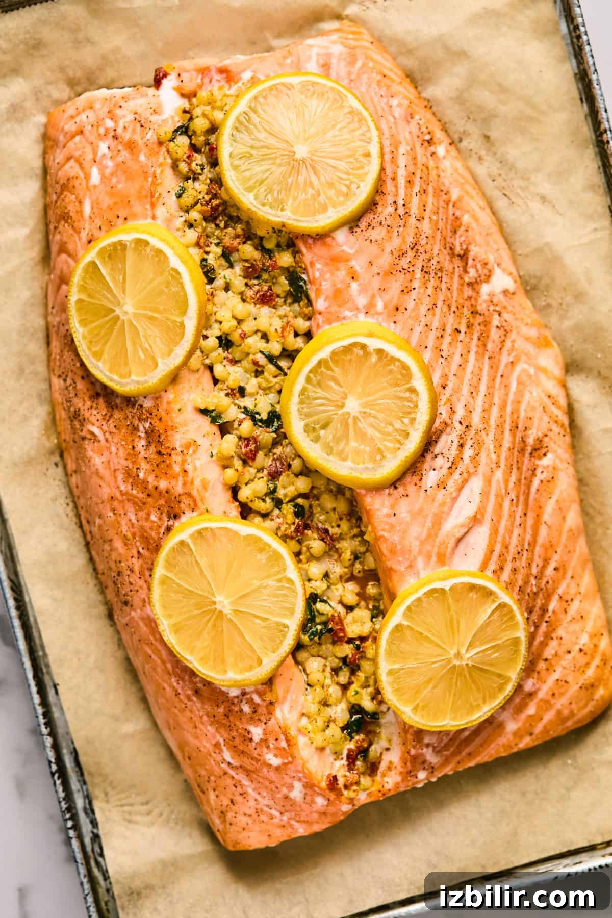 Baked salmon fillet stuffed with a mixture, topped with lemon slices on parchment paper in a baking tray.