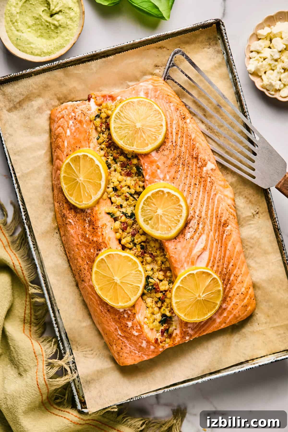 Baked salmon fillet stuffed with couscous and topped with lemon slices on a parchment-lined baking tray, with a spatula beside it.
