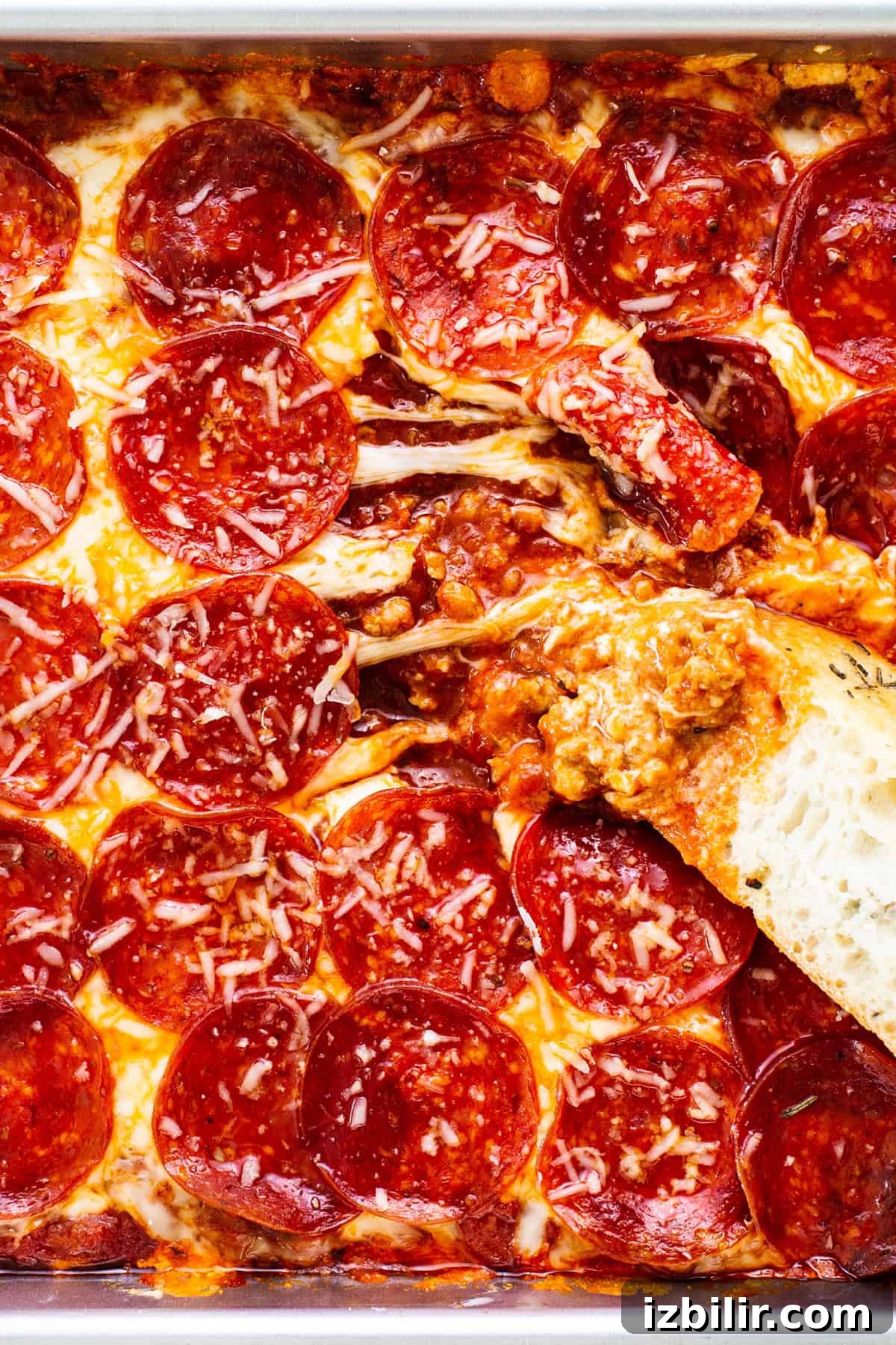Close-up of a pepperoni pizza dip with melted cheese, pepperoni slices, and a piece of bread dipped into the mixture.