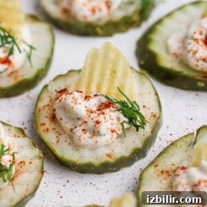 Close-up of pickle chip topped with creamy filling, garnished with dill and a potato chip piece.
