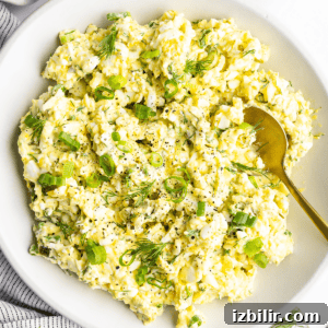 Creamy Cottage Cheese Egg Salad Recipe 6 A bowl of egg salad with chopped green onions and dill, accompanied by a gold spoon.