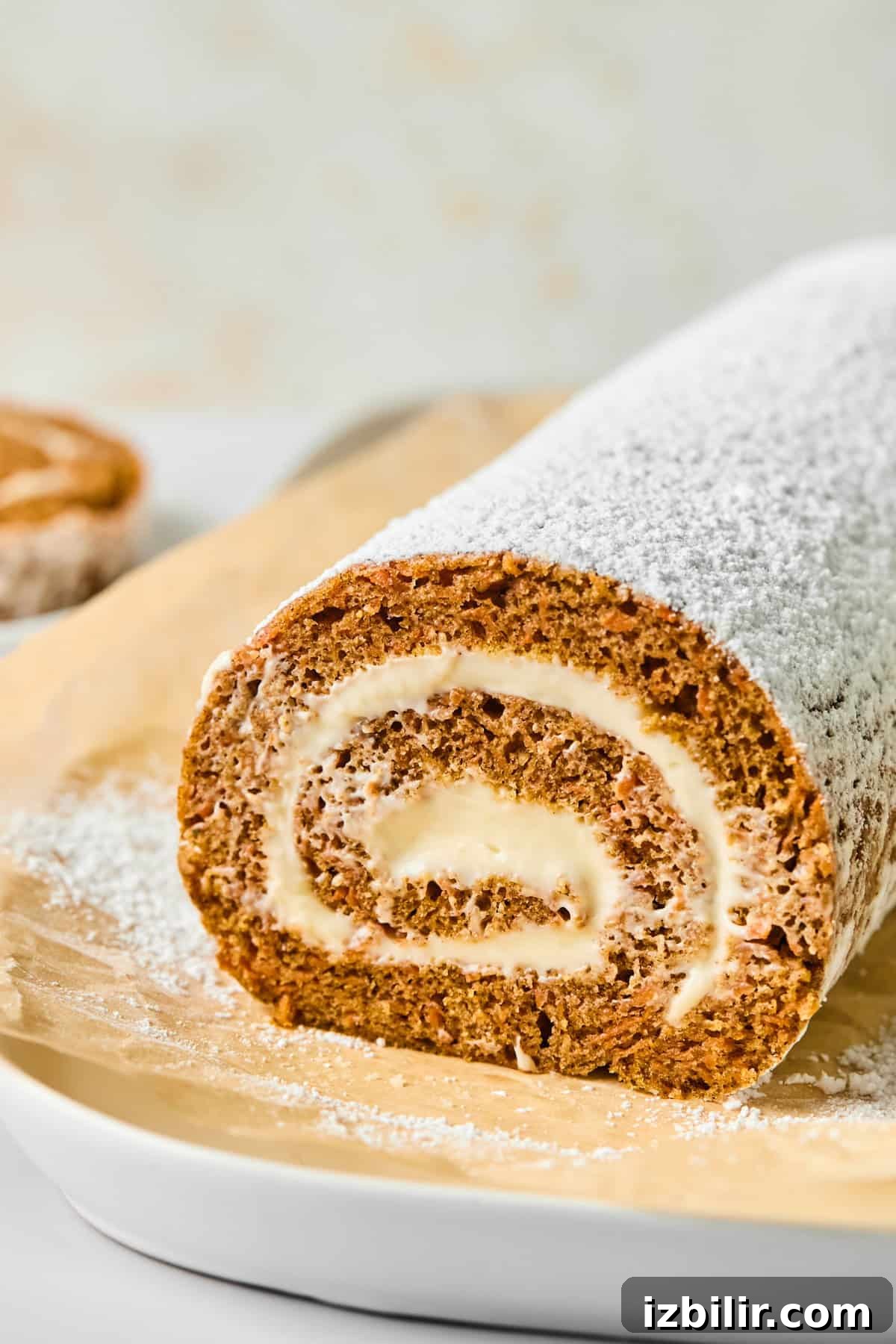 A rolled cake dusted with powdered sugar on parchment paper, showing a spiral of cream filling.