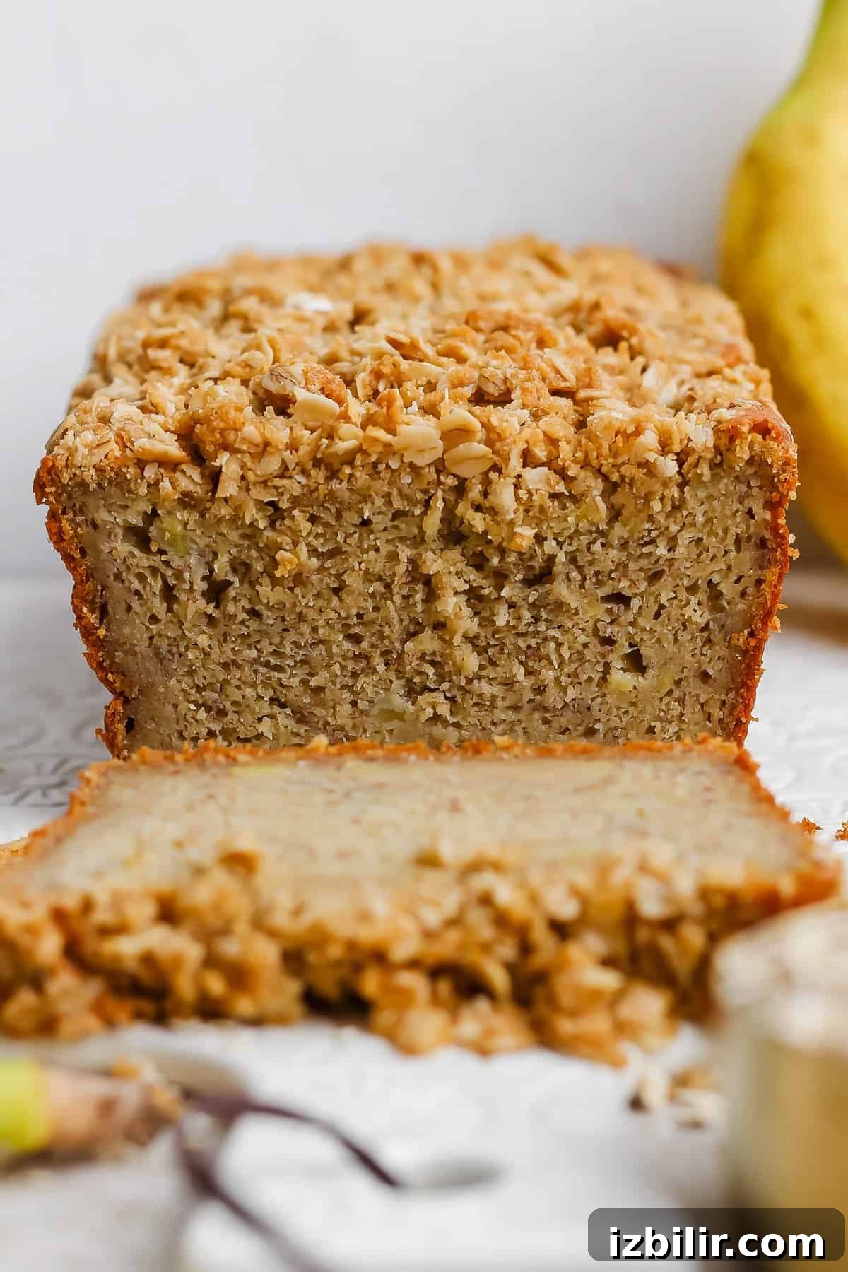 A sliced loaf of banana bread topped with a crumbly oat and nut mixture, placed on a white surface.
