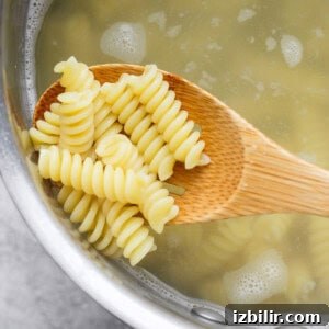 Roasted Red Pepper Pasta Salad with Cottage Cheese 7 A wooden spoon holding cooked rotini pasta above a pot of boiling water.