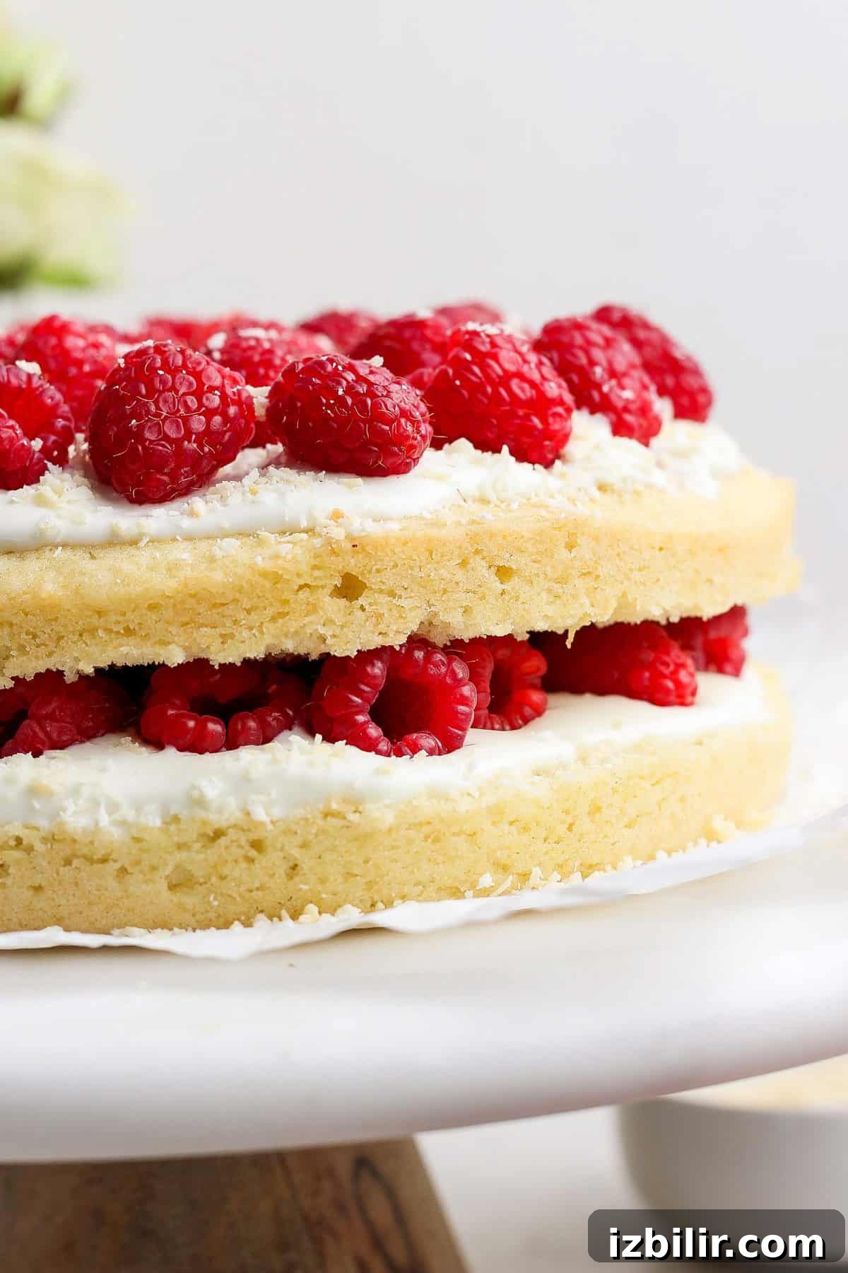 Layered cake with white frosting and fresh raspberries on a cake stand.