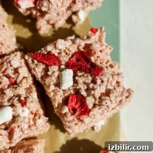 Rice crispy treat square with red dried strawberries and small marshmallows on a green and beige surface.