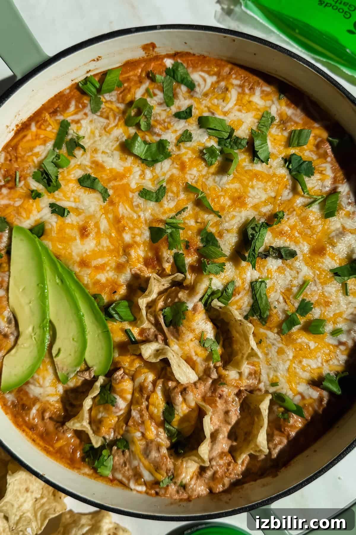 Creamy Ground Beef Queso with Cottage Cheese 2 A dish of cheesy dip topped with cilantro and avocado slices in a white casserole dish, surrounded by tortilla chips.