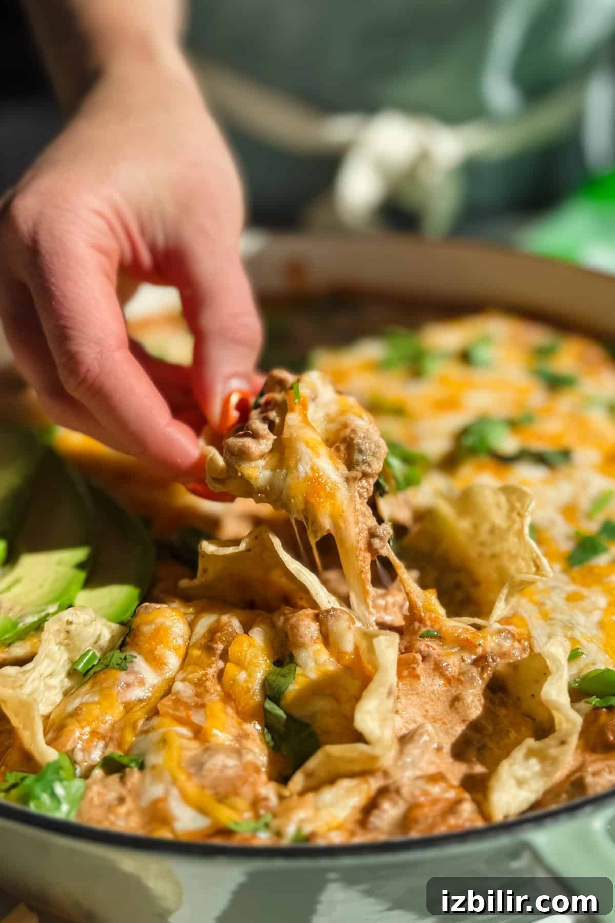 Creamy Ground Beef Queso with Cottage Cheese 3 Hand reaching into a dish of cheesy nachos topped with cilantro and sliced avocado.