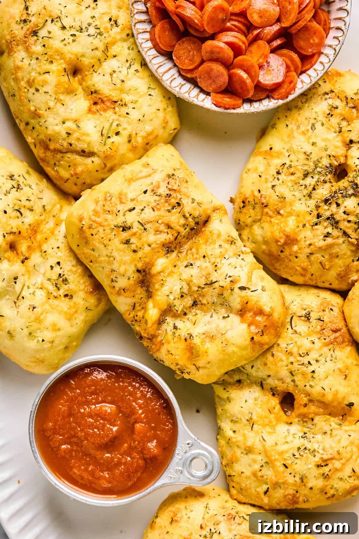 Homemade Protein-Packed Pizza Hot Pockets 2 Golden, herb-seasoned bread parcels resembling mini pizza hot pockets sit beside a small dish of sliced pepperoni and a cup of marinara sauce.